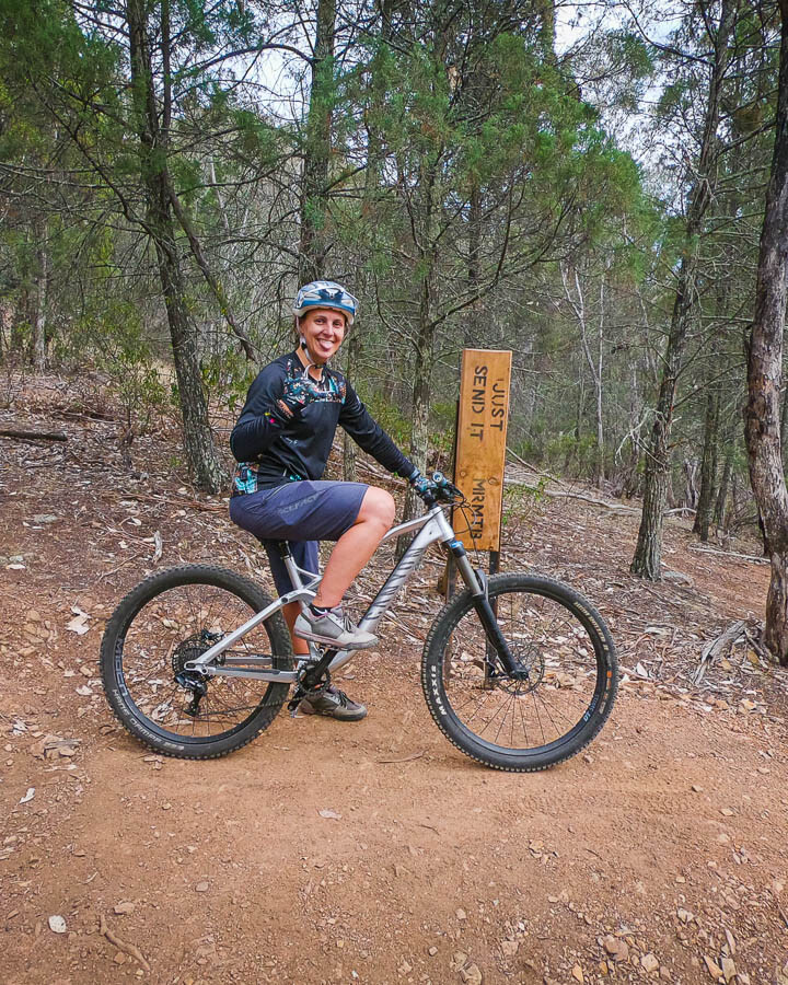 Candace sitting at the send it sign in Mudgee Mountain bike trails gravity runs