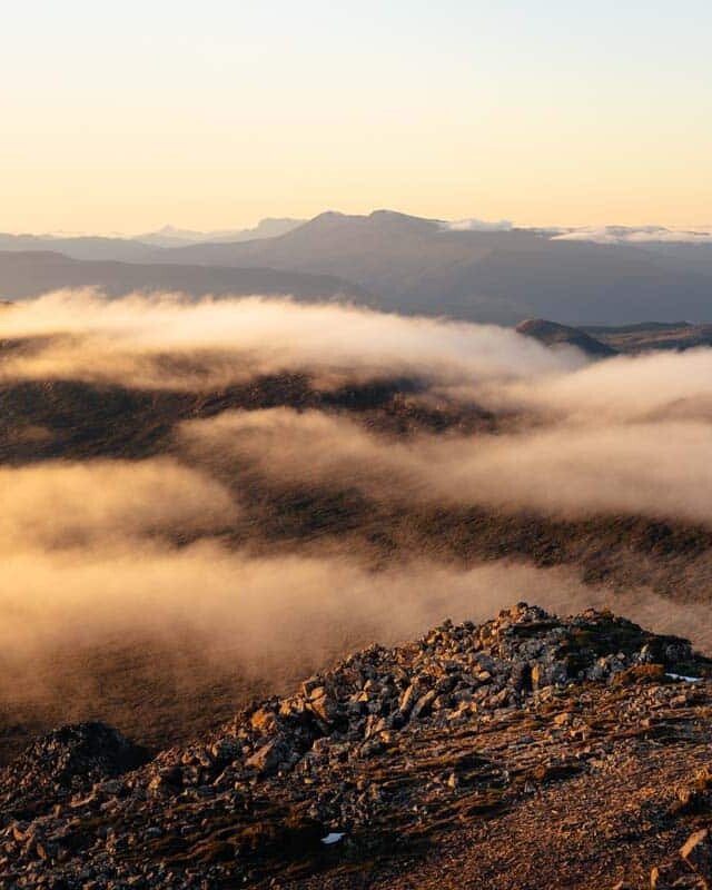 Cloud waterfall forming over Hartz Peak at sunset overlooking the distant mountain peaks of Hartz Mountains National Park
